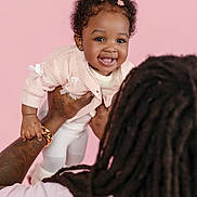 Malani joined the competition — help win amazing prizes! baby, child, smile, curly_hair, pink_background, pink_clothing, flower_clips, adult_hand, dreadlocks, holding, happy, portrait, cute, toddler, infant, studio, warmth, family, joy, love