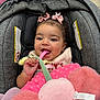 baby, child, car_seat, curly_hair, pink_bows, plush_toy, pink, gray, smiling, happy, infant, cute, toy, soft_texture, head_support, clothing, indoor, close_up, person, toddler