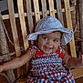 Tyla is registered to the contest to win money with this photo: baby, child, smiling, hat, dress, plaid, red, white, blue, wooden_chair, furniture, happy, sitting, indoors, person, cute, infant, portrait, arm, headwear