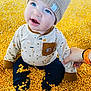 baby, child, blue_eyes, knitted_hat, corn_kernels, sitting, cute, curious, hand_holding, long_sleeve_shirt, pants, indoor, close_up, infant, soft_lighting, smiling, playful, yellow, warm_clothing, person