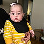 Mila Vardanyan joined the competition — help win amazing prizes! baby, black_bib, child, chubby_cheeks, closeup, clothing, cute, expressionless, face, hand, holding, human, indoor, infant, newborn, person, pink_bow, portrait, yellow_striped_onesie, young_child