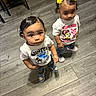 toddler, child, indoor, floor, wooden_floor, curly_hair, bow, tshirt, jeans, sneakers, standing, looking_up, person, footwear, casual_clothing, toy, chair, expression, cute, hair_accessory
