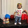 toddler, child, birthday, party, cake, balloons, gift_bags, table, shirt, jeans, sneakers, hand_holding, curtains, celebration, indoor, smiling, standing, person, mickey_mouse, minnie_mouse