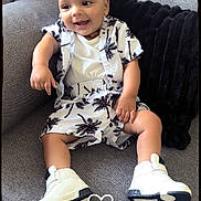 Ayaan a rejoint le concours — aidez-le/la à gagner de superbes lots ! baby, child, smiling, couch, clothing, white_shoes, shorts, shirt, tropical_print, indoor, pillow, happy, sitting, footwear, person, cute, comfortable, casual, fashion, infant