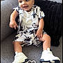 baby, child, smiling, couch, clothing, white_shoes, shorts, shirt, tropical_print, indoor, pillow, happy, sitting, footwear, person, cute, comfortable, casual, fashion, infant