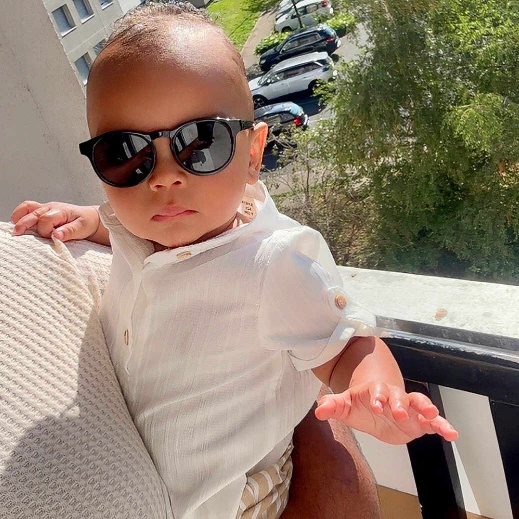 Ayaan participe au concours pour gagner de l'argent avec cette photo : adult_hand, apartment_buildings, baby, balcony, child, cool, cute, fashion, holding, outdoor, person, portrait, shade, striped_pants, summer, sunglasses, sunlight, trees, urban, white_shirt