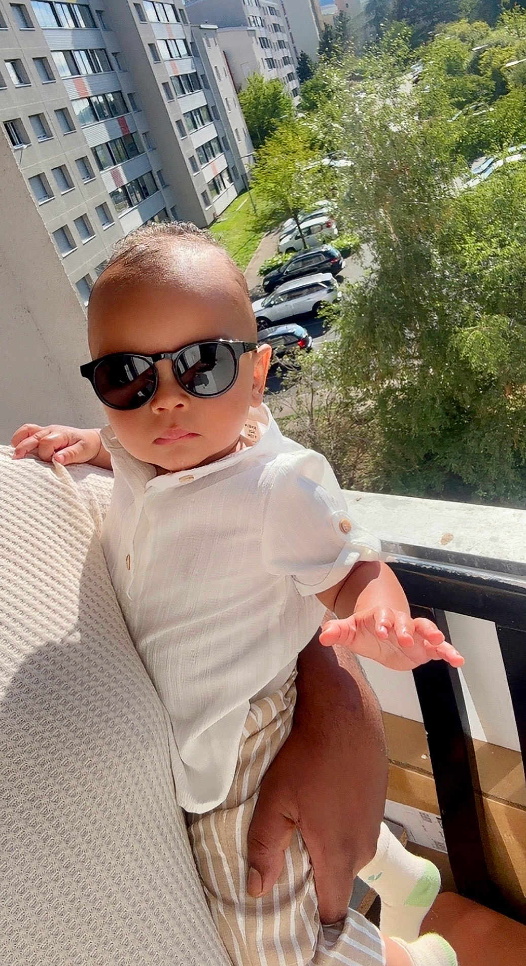 Ayaan participe au concours pour gagner de l'argent avec cette photo : baby, child, sunglasses, white_shirt, striped_pants, adult_hand, balcony, sunlight, trees, apartment_buildings, outdoor, portrait, fashion, cool, cute, person, summer, urban, holding, shade