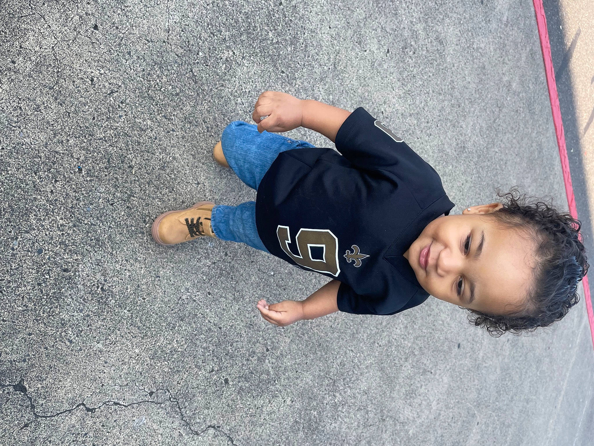 Caleb is registered to the contest to win money with this photo: asphalt, child, concrete, denim, flooring, foot, fun, grass, human_leg, joy, leg, leisure, person, plant, road, road_surface, shadow, sidewalk, sitting, tar