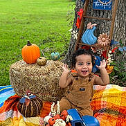 Tevita joined the competition — help win amazing prizes! autumn, blanket, child, decorations, fall, grass, happy, hay_bale, leaves, nature, outdoor, overalls, plaid, playful, pumpkins, smiling, thankful_sign, toddler, toy_truck, tree