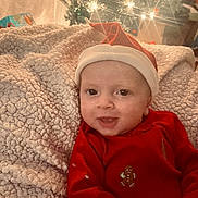 Nicolaos joined the competition — help win amazing prizes! baby, infant, face, smiling, red_clothing, santa_hat, blanket, christmas_tree, holiday, decorations, lights, festive, indoors, cozy, child, portrait, cute, seasonal, happy, celebration