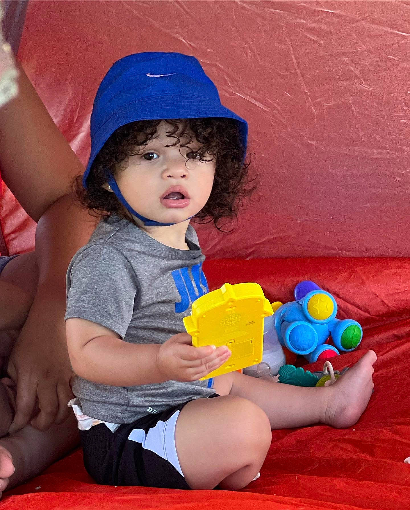 Isaias is registered to the contest to win money with this photo: arm, baby_playing_with_toys, baseball_cap, blue, cap, face, facial_expression, finger, fun, hand, happy, hat, leisure, person, pink, recreation, sun_hat, thigh, toddler, toy