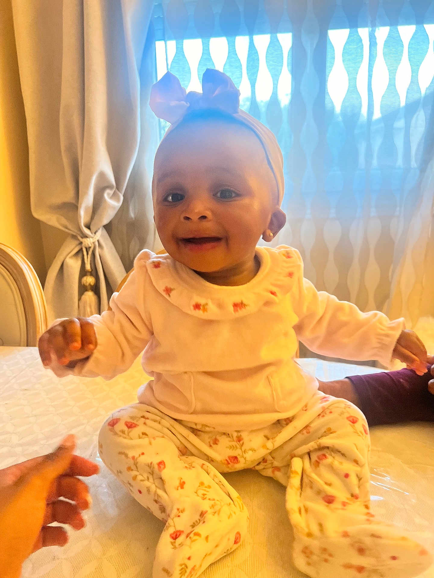 Maïwenn participe au concours pour gagner de l'argent avec cette photo : baby, infant, child, bow_headband, headband, smile, sitting, pajamas, floral_pattern, hand, earring, bed, curtain, window, indoors, portrait, cute, person, soft_lighting, happy