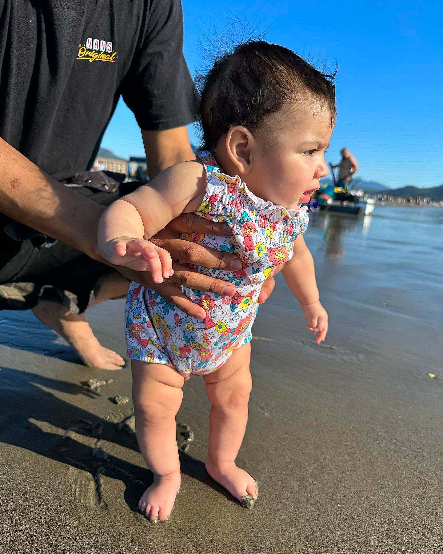 Armani is registered to the contest to win money with this photo: baby, barefoot, beach, event, foot, fun, gesture, happy, holding_hands, human_leg, leg, leisure, people_in_nature, people_on_beach, person, sandal, sky, thigh, toddler, tourism