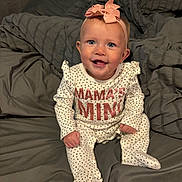 Ensley is registered to the contest to win money with this photo: baby, child, infant, smiling, headband, bow, polka_dot, onesie, bed, blanket, gray, happy, sitting, cute, indoors, portrait, face, blue_eyes, pink, clothing