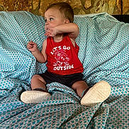 Johnathan is registered to the contest to win money with this photo: casual_clothing, child, comfort, couch, footwear, furniture, home_interior, indoor, looking_away, patterned_fabric, person, playful, portrait, red_tank_top, relaxed, sitting, small_shoes, stone_wall, toddler, young_child