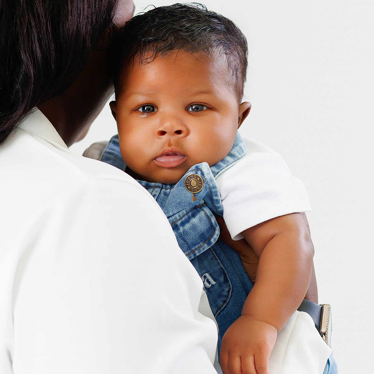 Jayce is registered to the contest to win money with this photo: baby, child, person, denim_overalls, white_shirt, holding, curly_hair, blue_eyes, skin, portrait, cute, infant, toddler, hand, face, adult, clothing, background, studio, expression