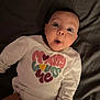 baby, infant, child, surprised, expression, face, eyes, mouth, clothing, shirt, text, hand, lying_down, blanket, indoor, portrait, cute, adorable, young, person