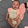 Reagan is registered to the contest to win money with this photo: baby, infant, smiling, onesie, pink_clothing, blanket, bed, happy, cute, face, person, skin, foot, hand, soft_fabric, lying_down, indoors, cozy, child, newborn