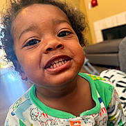 Jozaiah is registered to the contest to win money with this photo: animal_print, child, closeup, couch, cozy, curly_hair, cute, face, fireplace, furniture, happy, indoor, living_room, messy_face, pajamas, person, portrait, smiling, toddler, young_child