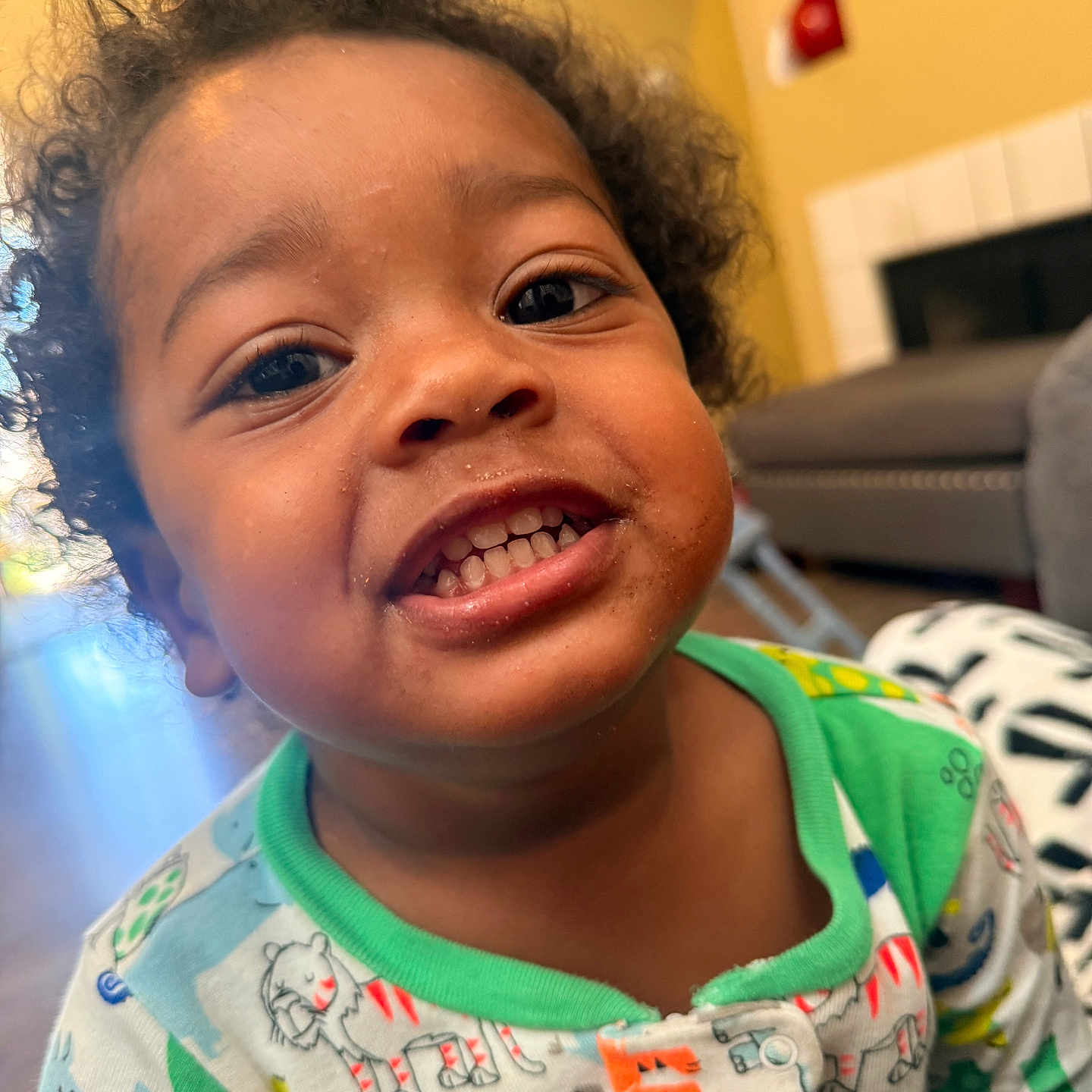 Jozaiah is registered to the contest to win money with this photo: animal_print, child, closeup, couch, cozy, curly_hair, cute, face, fireplace, furniture, happy, indoor, living_room, messy_face, pajamas, person, portrait, smiling, toddler, young_child