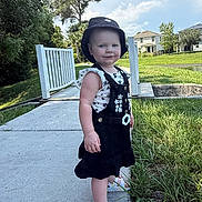 Gwendalyn is registered to the contest to win money with this photo: toddler, child, sidewalk, bridge, grass, tree, hat, sandals, outdoor, sunny, dress, person, smile, nature, residential_area, blue_sky, clouds, greenery, casual_clothing, footwear
