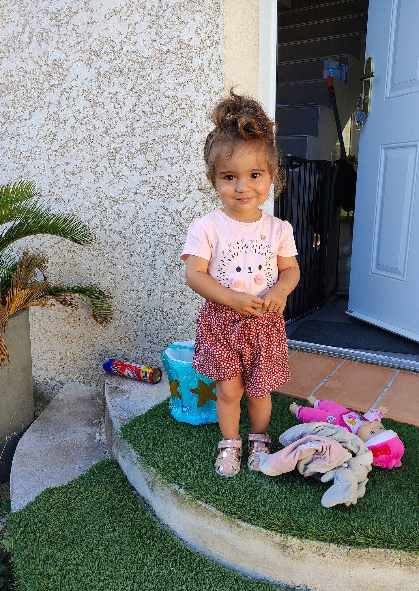 Angelina participe au concours pour gagner de l'argent avec cette photo : arecales, baby_toddler_clothing, child, door, floor, flooring, fun, grass, houseplant, joy, leisure, magenta, person, pink, plant, product, room, sandal, sitting, sneakers