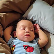 Dante is registered to the contest to win money with this photo: baby, sleeping, arms_up, curly_hair, blue_shirt, spiderman, iron_man, pillow, blanket, bed, cozy, child, infant, cute, peaceful, indoors, relaxed, soft_lighting, portrait, rest