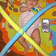 Dayana participe au concours pour gagner de l'argent avec cette photo : baby, play_mat, toy, rattle, play_gym, floor, wooden_floor, parquet, infant, child, indoor, colorful, padded_bars, clothing, foot, hand, red_eye, person, cute, lying_down