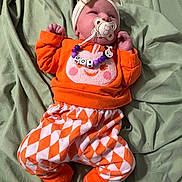 Lilith is registered to the contest to win money with this photo: baby, pacifier, headband, orange_clothing, patterned_pants, socks, blanket, infant, cute, lying_down, bed, child, face, sleepwear, toddler, soft_fabric, comfort, indoors, resting, person