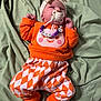baby, pacifier, headband, orange_clothing, patterned_pants, socks, blanket, infant, cute, lying_down, bed, child, face, sleepwear, toddler, soft_fabric, comfort, indoors, resting, person
