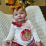 baby, child, smiling, bow, yellow_bow, christmas_tree, holiday, knitted_blanket, indoor, cute, portrait, sitting, clothing, patterned_pants, decorative_patch, festive, soft_lighting, happy, young_child, home