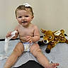 baby, child, diaper, bow, tissue, plush_toy, deer, medical_table, happy, smiling, cute, sitting, infant, indoor, skin, person, toy, playful, young, healthcare
