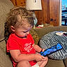 best_sister_ever, cat_face, child, couch, curly_hair, cute, diaper, focused, furniture, glasses, indoors, interior, lamp, person, pillow, red_shirt, sitting, smartphone, toddler, wood_paneling