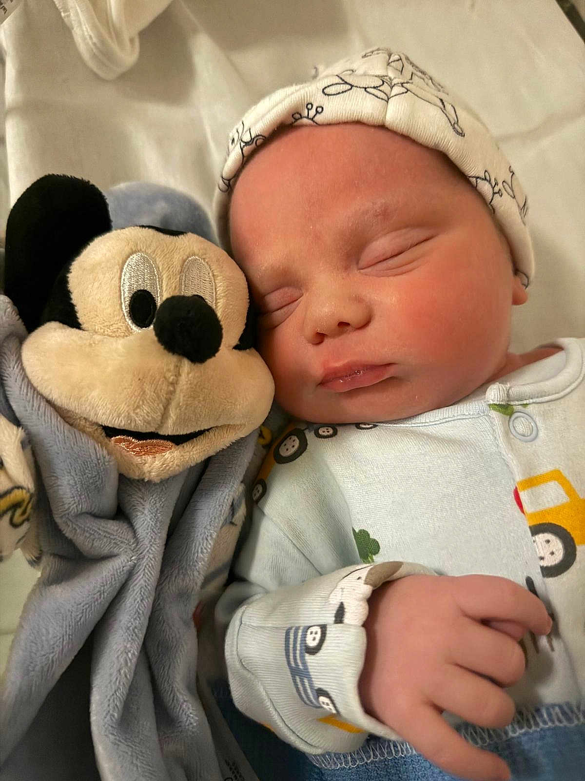 Hudson is registered to the contest to win money with this photo: baby, newborn, sleeping, plush_toy, mickey_mouse, soft_toys, hat, clothing, hand, bed, blanket, infant, cute, peaceful, portrait, child, toy, closeup, indoors, rest