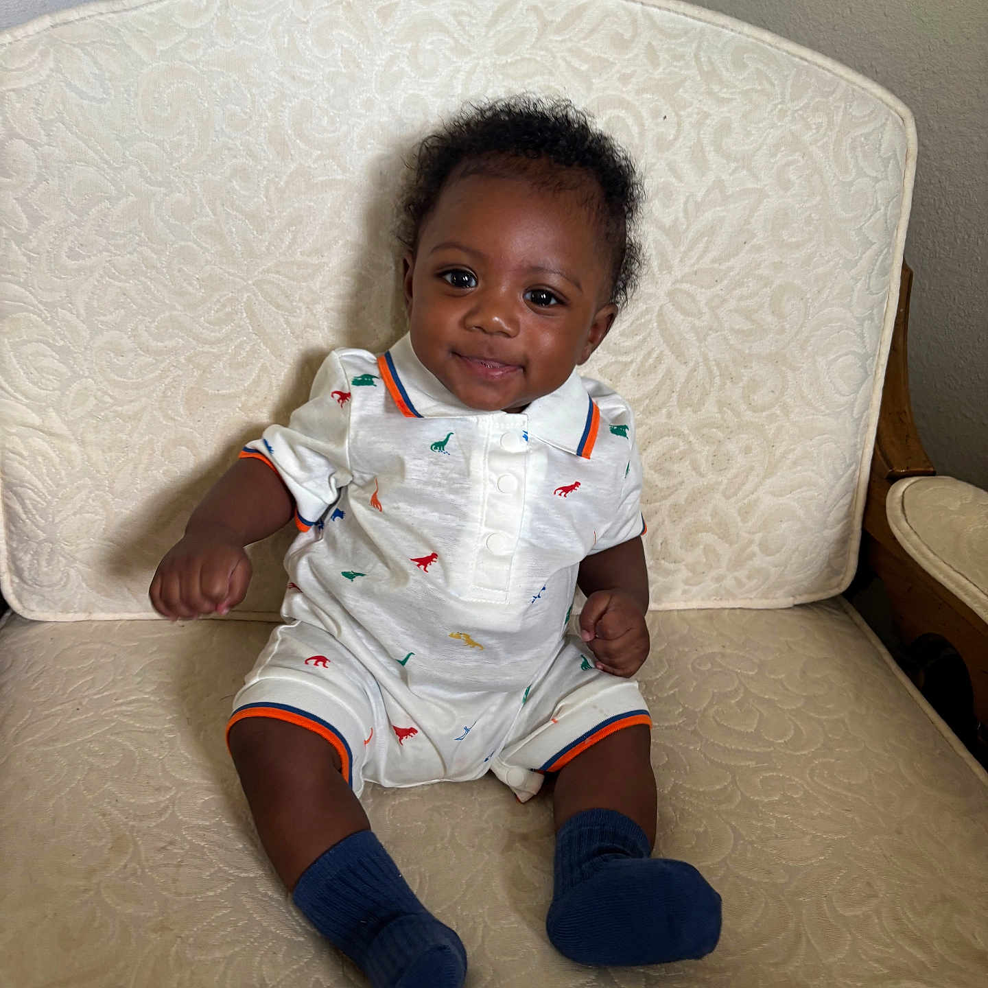 Raziel joined the competition — help win amazing prizes! baby, casual, chair, child, clothing, curly_hair, cute, dark_skin, dinosaur_print, furniture, happy, indoor, infant, patterned_fabric, person, portrait, sitting, smiling, socks, toddler