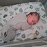 Ryan is registered to the contest to win money with this photo: baby, newborn, sleeping, crib, swaddle, gray_clothing, floral_pattern, mattress, pacifier, mesh_crib, infant, peaceful, indoors, head, face, person, resting, child, soft_lighting, quiet