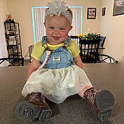 Kinsley joined the competition — help win amazing prizes! chair, child, cowboy_boots, denim_overalls, dining_area, face, flower, flower_vase, happy, headband, indoor, kitchen_counter, person, picture_frame, portrait, skirt, smiling, table, toddler, yellow_shirt
