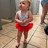 Kinsley joined the competition — help win amazing prizes! adult, ankle_band, barefoot, casual, child, clothing, curious_expression, hair, indoor, locker_room, looking_up, person, red_tutu, shorts, skin, sneakers, standing, swimsuit, tile_floor, toddler