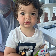 Marty is registered to the contest to win money with this photo: toddler, child, curly_hair, smoothie_pouch, white_tshirt, older_man, lap, outdoor, porch, daylight, expression, holding, greenery, casual_clothing, person, face, looking_at_camera, seated, cute, summer