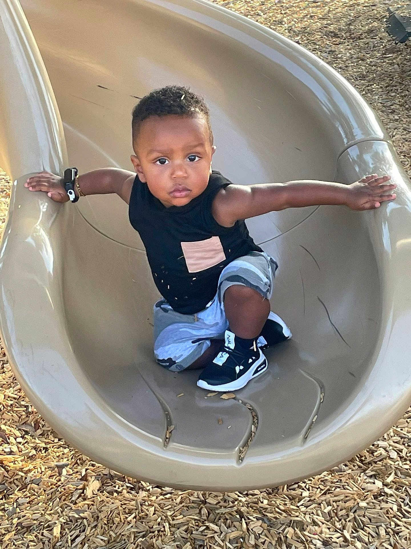 Justin joined the competition — help win amazing prizes! toddler, child, slide, playground, outdoor, wood_chips, black_shoes, black_shirt, shorts, arms_outstretched, determined_expression, daylight, play, fun, park, casual_clothing, active, young_child, person, recreation