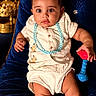 baby, blue_necklace, child, comfortable, cream_outfit, curious_eyes, cute, decorative, expression, furniture, golden_decor, indoor, infant, luxury, playful, portrait, sitting, toy, velvet_chair, young_child