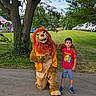 Keith is registered to the contest to win money with this photo: child, boy, mascot, lion_costume, pokemon_tshirt, outdoor, grass, tree, sidewalk, park, greenery, summer, casual_clothing, costume, character, smile, fun, event, nature, people