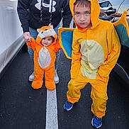 Keith is registered to the contest to win money with this photo: child, costume, orange, parking_lot, person, adult, hoodie, jeans, shoes, car, smile, wings, baby, holding_hands, asphalt, line, hood, outdoor, cute, playful