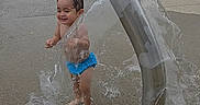 Alex joined the competition — help win amazing prizes! barefoot, bench, blue_swim_diaper, child, concrete, daytime, fun, grass, happy, outdoor, park, playground, smiling, splash_pad, summer, toddler, tree, water, water_spray, wet