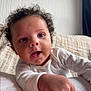 Ellis is registered to the contest to win money with this photo: baby, child, close_up, couch, curiosity, curly_hair, cute, expression, face, hand, happy, indoor, infant, person, portrait, skin, smiling, texture, white_clothing, young_child