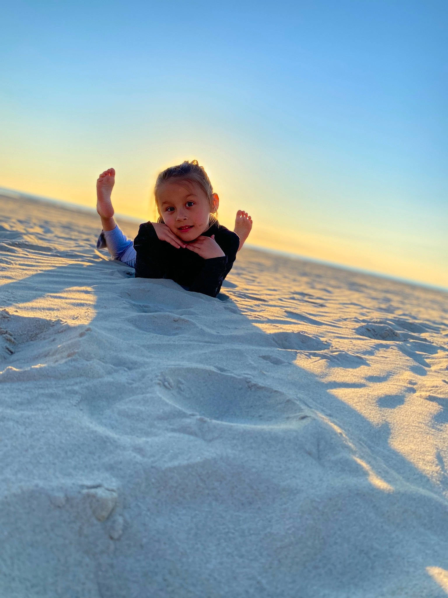 Inaya a rejoint le concours — aidez-le/la à gagner de superbes lots ! aeolian_landform, child, dusk, freezing, fun, gesture, happy, horizon, landscape, leisure, people_in_nature, people_on_beach, person, personal_protective_equipment, recreation, sand, shadow, sky, smile, toddler