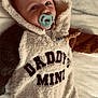 baby, child, pacifier, hooded_onesie, text_on_clothing, fluffy_texture, blanket, soft_fabric, infant, cute, sleepwear, lying_down, indoors, warm_clothing, newborn, face, head, person, comfort, expression