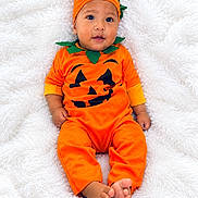 Xaiden is registered to the contest to win money with this photo: baby, infant, child, pumpkin_costume, halloween, orange_clothing, green_leaves, hat, costume, portrait, lying_down, blanket, fluffy_blanket, indoors, cute, wide_eyed, smiling, bare_feet, seasonal, photography