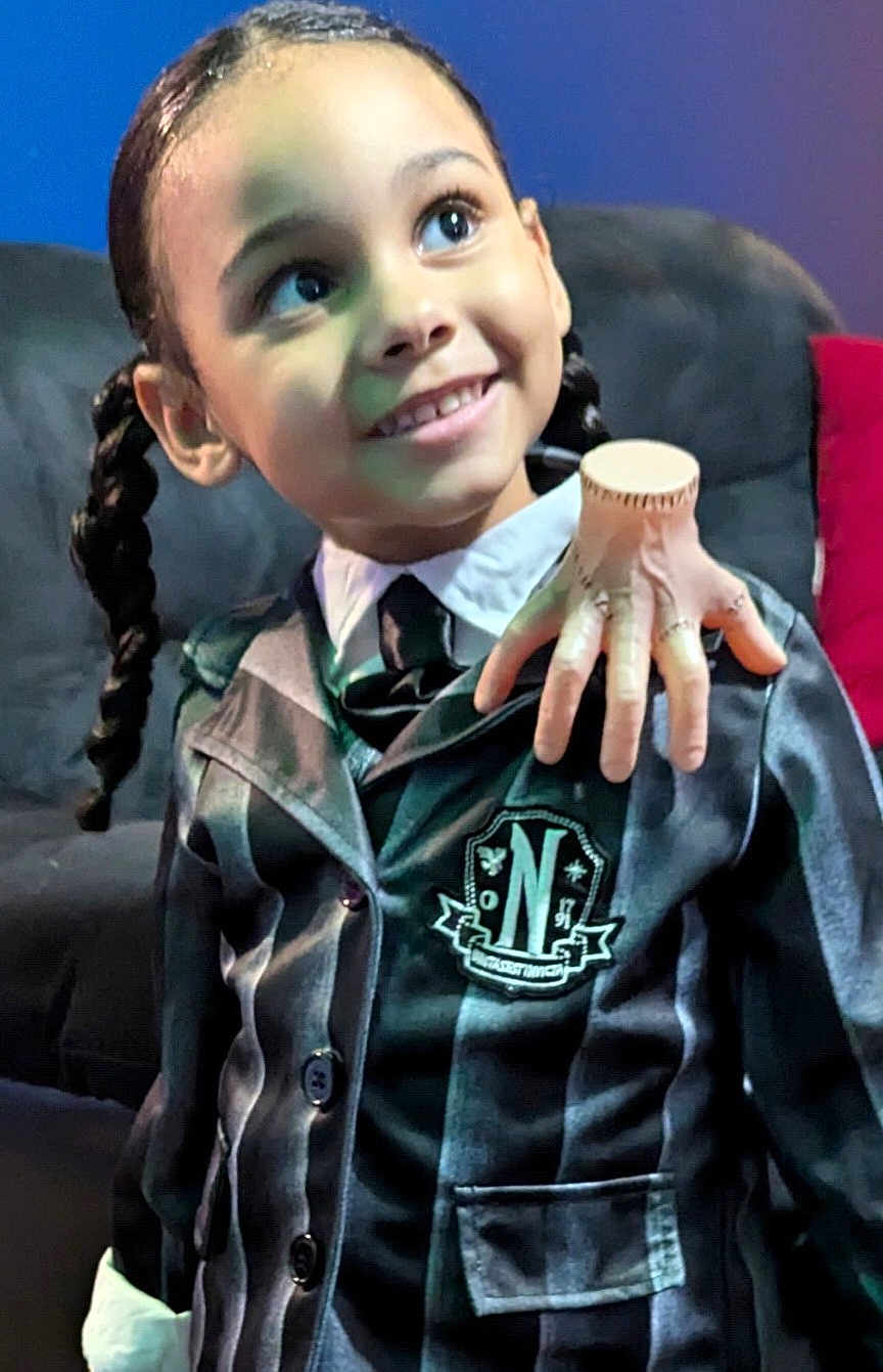 Brooklynn joined the competition — help win amazing prizes! child, smile, braids, fake_hand, jacket, striped_clothing, couch, indoor, portrait, happy, young, face, person, costume, hand_prop, black_hair, buttoned_jacket, background, seated, looking_away