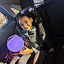 child, car_seat, smiling, seatbelt, purple_container, sunlight, car_interior, window, happy, young_person, clothing, portrait, seat, daylight, safety, child_safety, vehicle, casual, childhood, inside_car